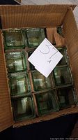 Set of 12 green-tinted glass votive holders packed in a brown cardboard box.