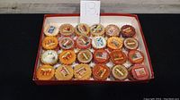 Top-down view of 24 assorted Yankee Candle scented wax tarts in orange, brown, white, yellow, and red hues in a red tray with labels visible.