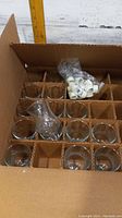 Box containing 14 clear peg glass votive holders and a plastic bag of white caps or lids.