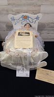 Full view of the Snow White doll lying in the white wooden cradle with certificate on her dress in front.