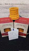 Three new boxed ceramic votive candle crocks with one used displayed in front, all yellow-orange and embossed with vine pattern