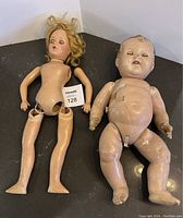 Both vintage dolls laid on flat surface: baby doll on the right with worn composition body, the other doll to the left missing limbs, hair messy.