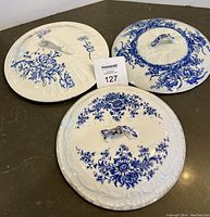 Top view of three round ceramic chamber pot lids with different blue floral patterns on a white background, showing their raised handles.
