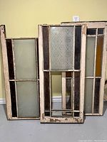 Three vertical antique church windows with wood frames showing distressed paint and varying glass panes including frosted and stained glass.