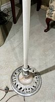 Close-up of the antique floor lamp's base showing the marble center and decorative metal base with ribbed pole.