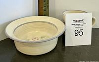Cream-colored ceramic bowl with floral accents, photographed with a ruler for size reference.