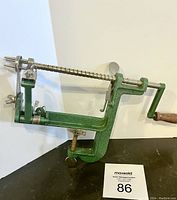Green cast metal apple peeler with wooden handle attached to clamp base, showing side profile and working clamp mechanism