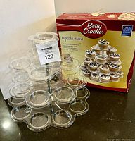 Three-tier clear plastic cupcake stand displayed next to its original Betty Crocker box showing the stand and box together.