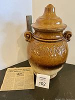 Full view of the Rumtopf pot with lid, showing embossed cursive 'Rumtopf' and the brown gradient finish, alongside a typed recipe clipping.
