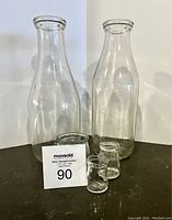 Two large vintage clear glass milk bottles standing behind in the lot
