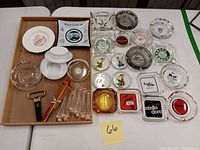 Full lot overview showing assorted glass and ceramic ashtrays, cocktail muddlers, and bar tools on a tray and table.