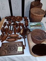 Full view of wooden kitchen items and woven baskets on a white tablecloth, showing various goblets, bowls, carvings, and baskets