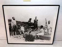 Framed black and white photograph showing full image of eight beach goers in vintage bathing suits, with rocky beach background and a small rowboat.