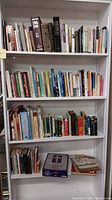 Wide view of bookshelf with multiple rows of books on various subjects including religion, art, health, and cooking.
