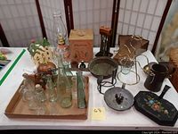 Overview of lot showing bottles, Christmas house, oil lamps, metal pan, canister set, and other metalware on table