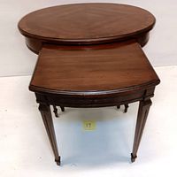 Stacked oval wood nesting tables with dark finish and tapered legs, large table on bottom and smaller table nested inside