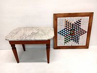 Side view of small wooden side table with white marble top and a framed colorful tiled Chinese checkers game board leaning against the wall.