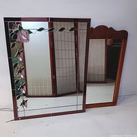 Both mirrors together showing the stained glass style floral mirror on the left and the wood framed mirror with scalloped top on the right.