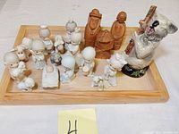 Photo showing full lot of Precious Moments nativity figurines, two wooden carved human figures, and a large ceramic bear figurine on a wooden tray.