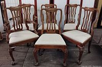 Front view of six Roberto Barahona dining chairs showing upholstery, carved leg and foot details, and chair backs.