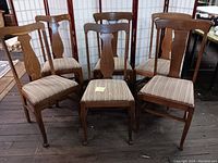Set of six oak T-back dining chairs arranged in two rows on a wooden floor with visible scratches and upholstery fabric on seats.