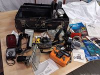 Wide shot showing the two underwater cameras, black carrying case, multiple flash units, mounting bracket, instruction manuals and other gear spread out on a wooden surface.