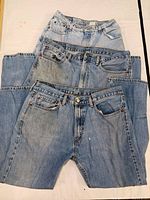 Three pairs of vintage Levi's jeans stacked, showing full length and classic light blue denim color with rivets and pockets.