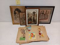 Lot showing four framed vintage prints grouped together, with a scrapbook and loose vintage greeting cards laid in front