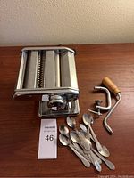 Photo of Amfa pasta maker with clamp, wooden hand crank, and set of ten stainless steel spoons on wooden surface