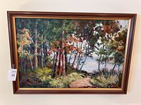 Frontal image of the framed oil painting showing a wooded landscape with a path and water in the background.