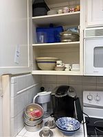 Kitchen cabinet and counter items including Keurig coffee machine, cups, bowls, tins, and water filter pitcher.