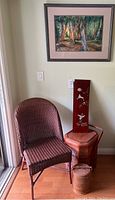 Wicker chair next to basket stack with tall decorative panel and framed wooded landscape artwork on wall