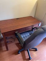 Photo showing the wooden desk with two drawers and gray office chair positioned in front of it.