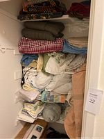Photo of hall closet showing stacked folded bedding including quilts, blankets, and sheets on shelves.