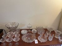 Complete Fostoria glassware collection displayed on table including bowls, stemmed glasses, plates, and small dishes all in clear glass with textured geometric pattern.