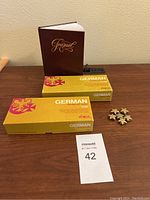Two boxes of German vocabulary cards, a brown journal, and a set of gold star pins arranged on a wooden surface.