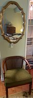 Wooden chair with green upholstered seat and cane backrest positioned below a decorative gold-framed mirror on the wall.