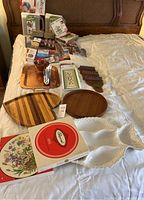 Overview of wooden trays, ceramic dishes, placemats, and decorative kitchen items spread on a bed.