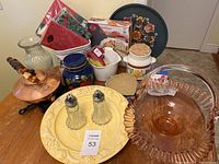 Wide angle photo showing multiple kitchen household items including copper kettle, yellow ceramic plate with salt & pepper shakers, blue floral canister, pink depression glass bowl, white ceramic jar, and other kitchen containers and trays.