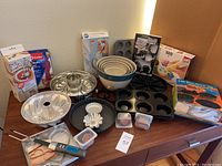 Wide view of the entire baking set on wooden surface including baking pans, mixing bowls, thermometer, and packaging boxes in background.