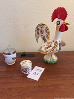 Photo of ceramic rooster figurine, white ceramic jar with a bird design and silver lid, and small lidded sugar bowl next to maxsold lot card