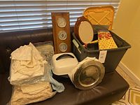 Full view of household items including chargers, tablecloths, thermometer panel, white kitchen appliance, and plastic container with miscellaneous items.