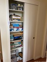Image showing the closet with sliding door partially open, revealing several shelves of office supplies including boxes of paper, plastic containers, and desk organizers.