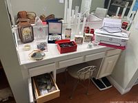 Vanity area countertop with arranged items including clocks, jewelry boxes, mirror, and other vanity items visible on white tile surface with drawer open below and stool seating