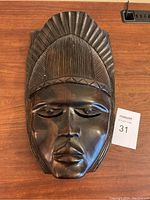 Front view of the carved African wood mask showing detailed facial features and ornate hair design.