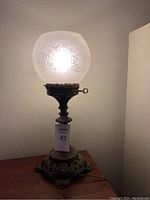 Full view of the lit vintage lamp showing frosted glass globe with floral etching and ornate metal base.