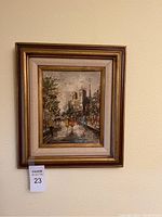 Full view of framed painting showing city street scene with pedestrians and historic building, hung on a beige wall.