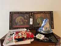 Full view of two framed western-themed prints, ceramic frog figurine, trays and botanical coasters/napkins on wooden surface