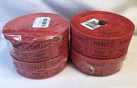 Four rolls of red double raffle tickets, three rolls sealed in plastic, one unsealed.