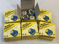 Six yellow boxes labeled Buss Fusetron Dual-Element Fuse Type TC 15, each box containing four fuses, arranged in opened boxes.